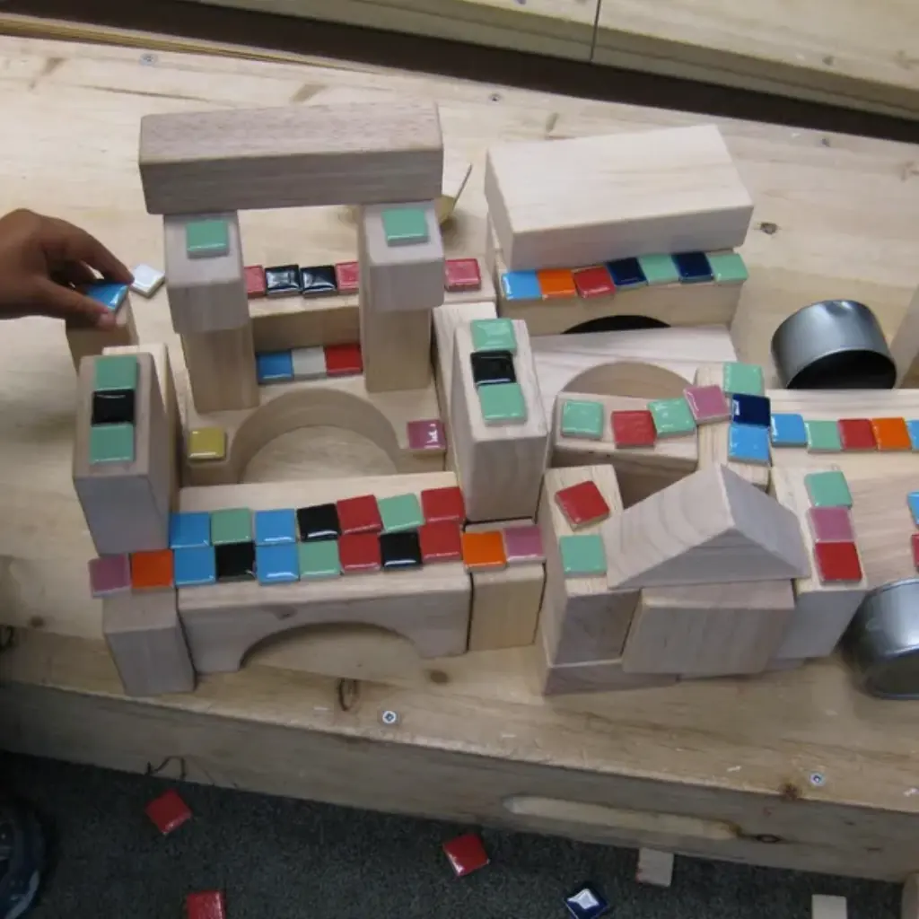 Blossoms Academy post: a child's hand placing tiles on a wooden block tower
